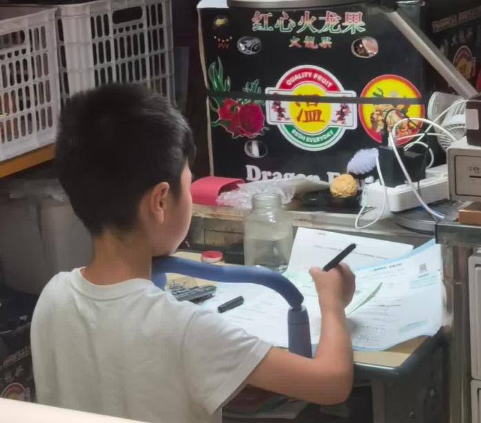 爆红！武汉江汉路闹市水果摊，一小学生背对人群专注写作业，全程头都不回，网友：我娃一张纸掉地上都要看